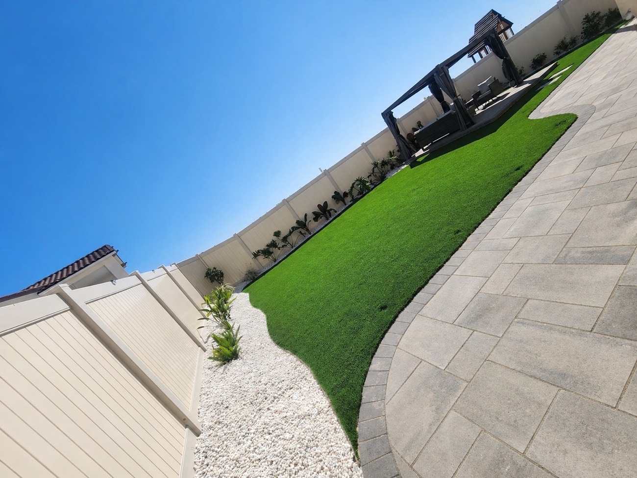 Artificial turf lawn curving alongside a paver walkway with a gravel border